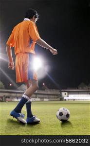 Rear view of man about to kick ball at soccer field