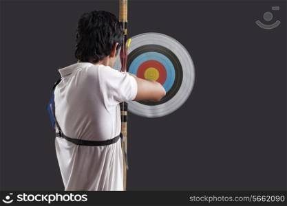 Rear view of man aiming target with bow against black background Rear view of man aiming target with bow against black background