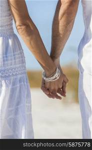 Rear view of man and woman romantic couple in white clothes holding hands on a deserted tropical beach with bright clear blue sky