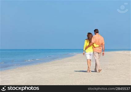 Rear view of man and woman romantic couple in white clothes walking on a deserted tropical beach with bright clear blue sky