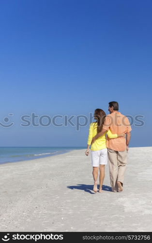 Rear view of man and woman romantic couple walking on a deserted tropical beach with bright clear blue sky