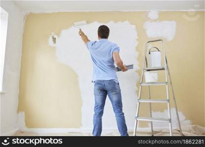 Rear View Of Man Painting Wall In Room Of House With Paint Roller