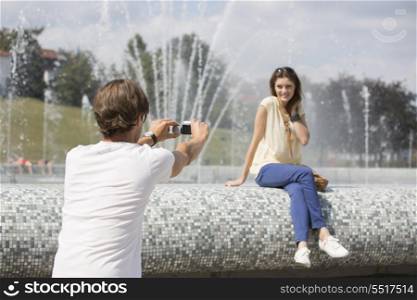 Rear view of man videotaping woman against fountain