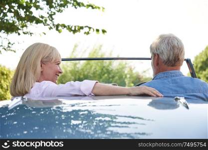 Rear View Of Mature Couple Enjoying Road Trip In Classic Open Top Sports Car Together
