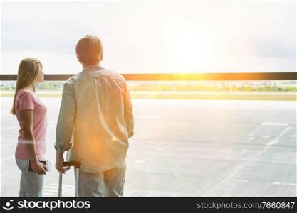 Rear view of mature man looking through the window with his daughter in airport