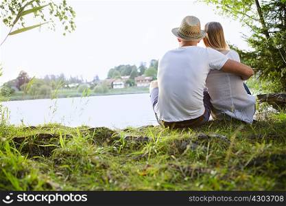Rear view of mid adult couple sitting by lake