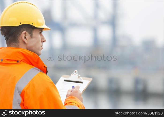 Rear view of mid adult man writing on clipboard in shipping yard
