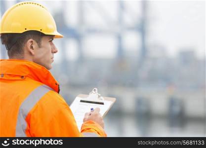Rear view of mid adult man writing on clipboard in shipping yard