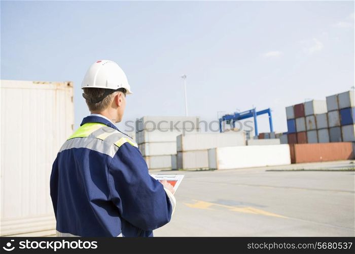 Rear view of middle-aged worker with clipboard in shipping yard
