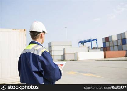 Rear view of middle-aged worker with clipboard in shipping yard