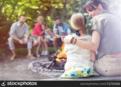 Rear view of mother sitting with arm around daughter while camping at park