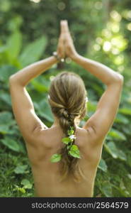 Rear view of nude Caucasian mid-adult woman with hands overhead in yoga pose.