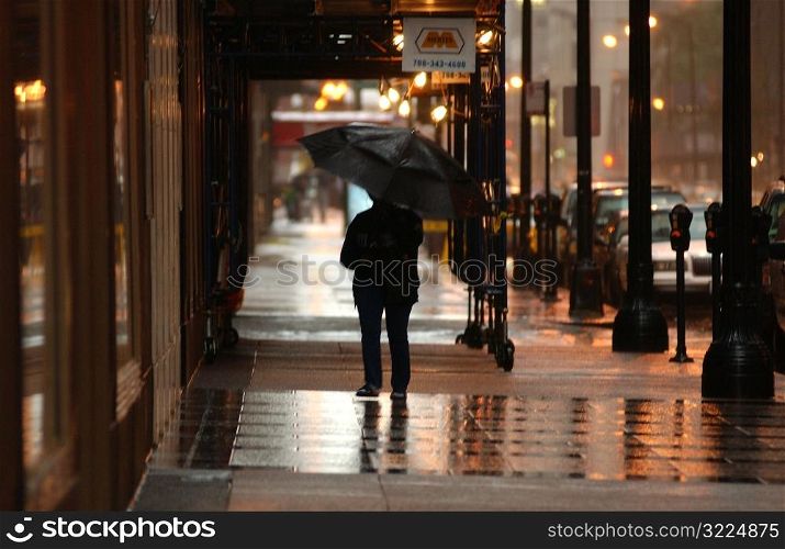 Rear view of person with an umbrella walking on the sidewalk