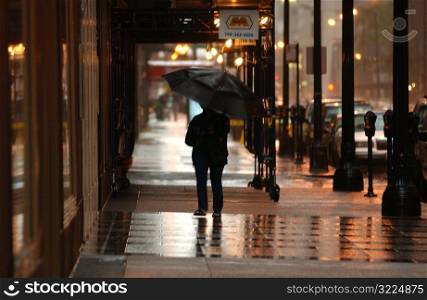 Rear view of person with an umbrella walking on the sidewalk