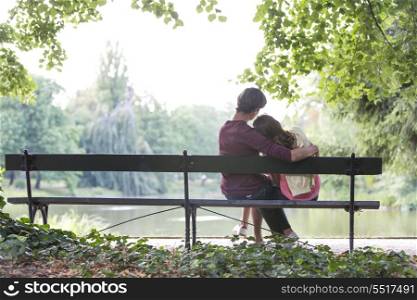 Rear view of romantic young couple sitting on bench at lakeside