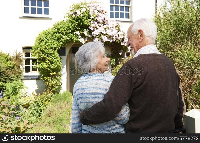 Rear View Of Senior Couple Outside Pretty Cottage