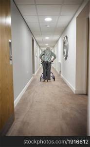 Rear View Of Senior Woman With Walker Walking Along Corridor In Retirement Home