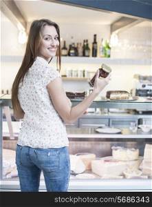 Rear view of smiling woman holding chocolate jar in front of display cabinet at cafe