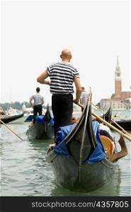 Rear view of three gondoliers standing on gondolas, Venice, Veneto, Italy