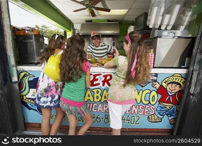 Rear view of three teenage girls talking to a bartender in a juice bar