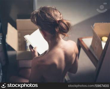 Rear view of topless woman sitting on the floor at home and putting stuff in a cardboard box