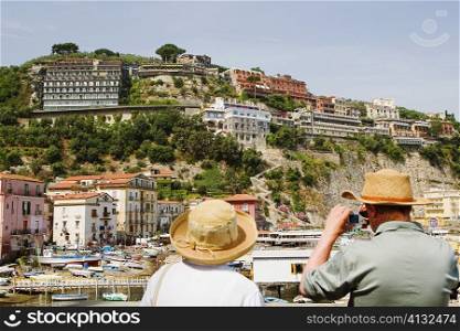Rear view of tourists photographing a harbor, Marina Grande, Capri, Sorrento, Sorrentine Peninsula, Naples Province, Campania, Italy