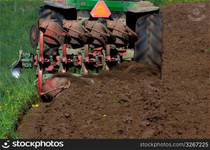 Rear view of tractor digging and tilling the earth on farm preparing for planting