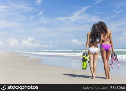 Rear view of two beautiful young women in bikinis with snorkel, mask &amp; flippers embracing on a deserted beach with blue sky