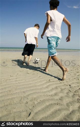 Rear view of two boys playing with a soccer ball on the beach