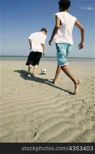 Rear view of two boys playing with a soccer ball on the beach