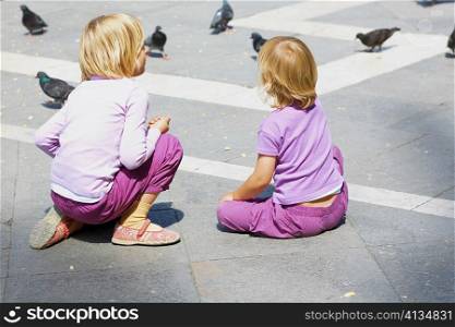 Rear view of two girls looking at pigeons, Venice, Veneto, Italy