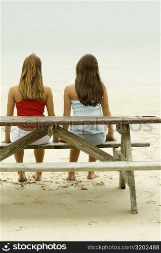 Rear view of two girls sitting on a bench at the beach