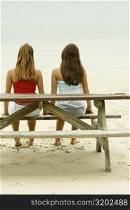Rear view of two girls sitting on a bench at the beach