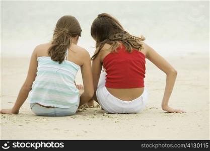 Rear view of two girls sitting on the beach
