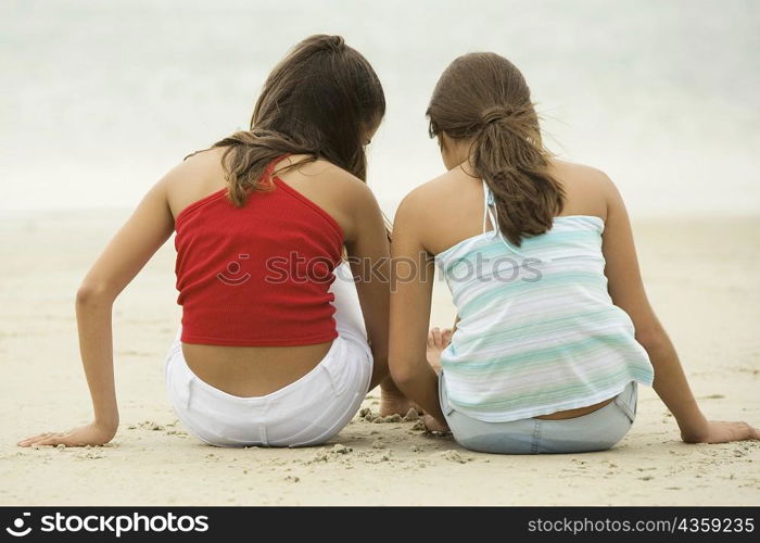 Rear view of two girls sitting on the beach