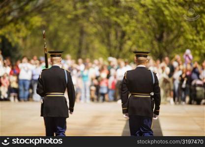 Rear view of two honor guards in front of a large group of people