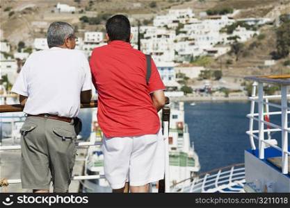 Rear view of two men leaning against a railing of a yacht and looking at view, Patmos, Dodecanese Islands, Greece
