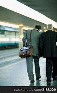 Rear view of two men walking at a railroad station platform, Rome, Italy