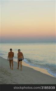 Rear view of two men walking on the beach