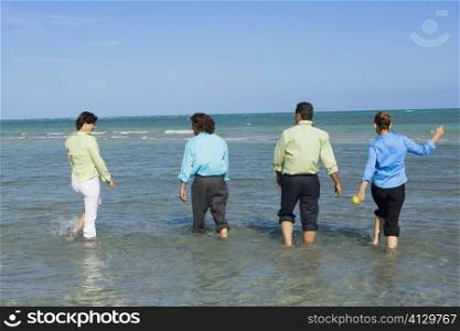 Rear view of two mid adult couples wading on the beach