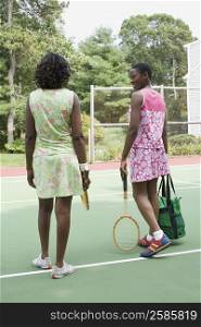 Rear view of two mid adult women holding tennis rackets in a court