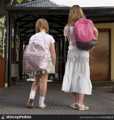 Rear view of two schoolgirls carrying schoolbags and walking