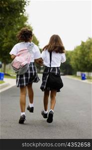 Rear view of two schoolgirls walking with holding hands