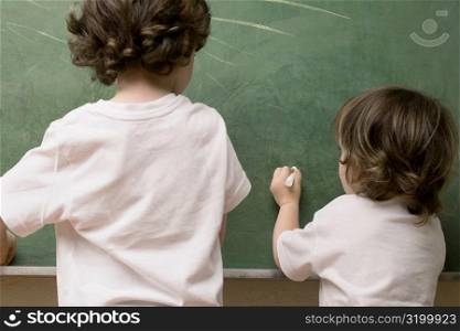 Rear view of two students drawing on a blackboard