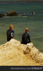 Rear view of two women sitting on a rock by the sea