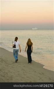 Rear view of two women walking on the beach