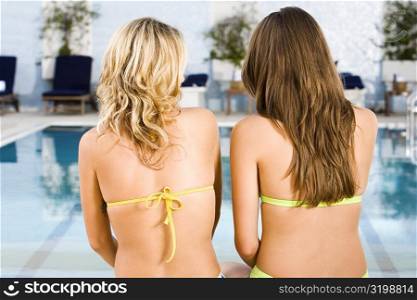 Rear view of two young women sitting at the poolside