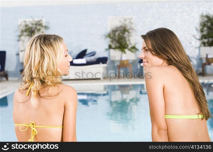 Rear view of two young women sitting at the poolside