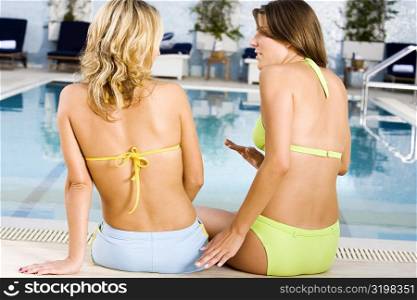 Rear view of two young women sitting on a bench at the poolside