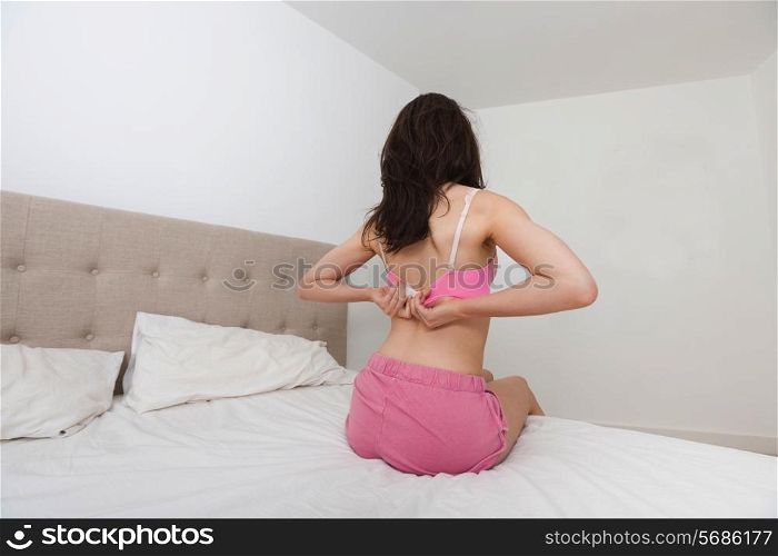Rear view of woman fastening bra in bed